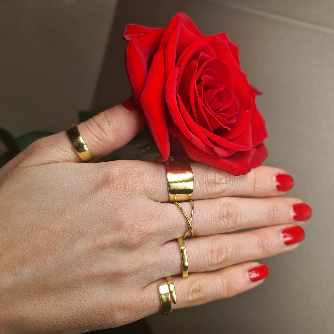 model with painted nails holding a rose with 5 adjustable 14k gold rings on